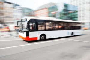 A city bus, one of the transport options in Noosa, is in motion, depicted with a motion blur effect to emphasize speed, traveling through a busy urban street with blurred buildings in the background.
