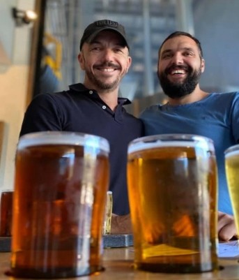 Two men smiling in front of a group of beers during a private tour.