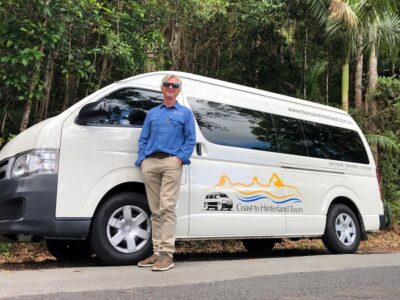 A man standing next to a white van in a forest on the Sunshine Coast.