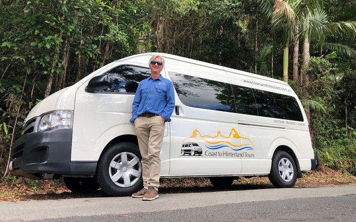 A man standing next to a white van in a forest on the Sunshine Coast.